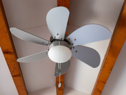 Ceiling fan with five alternating gray and white blades, a central light fixture, and pull chains, mounted on a ceiling with exposed wooden beams.