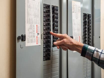 A person adjusts a breaker switch inside an open electrical panel mounted on a wall.