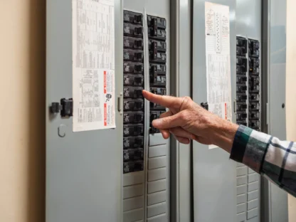 A person adjusts a breaker switch inside an open electrical panel mounted on a wall.