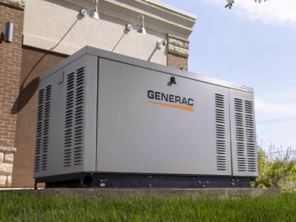 Large Generac generator on a concrete pad beside a building, surrounded by grass, with trees partially visible above.