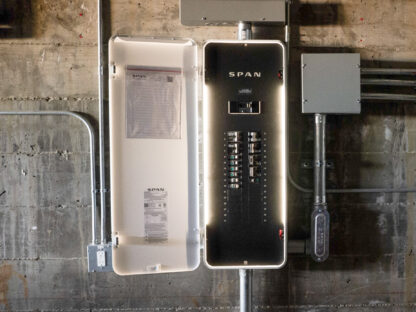 An open electrical panel attached to a wall with labeled switches and wiring visible.