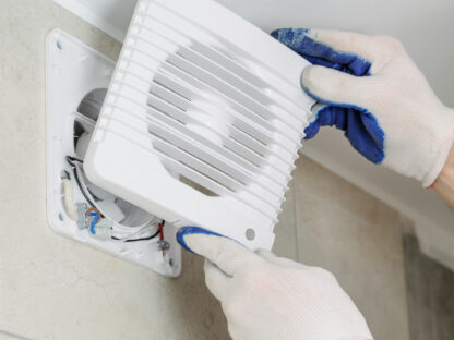 Person wearing gloves installs a white vent cover on a wall.