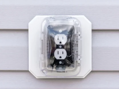 Outdoor electrical outlet with cover mounted on a vinyl siding wall.