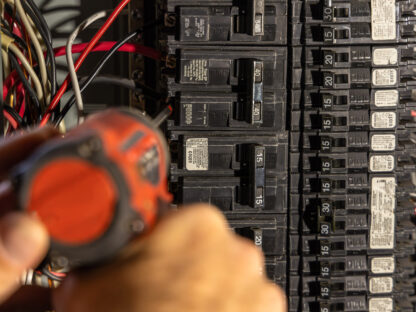 Person using a screwdriver to work on an electrical circuit breaker panel.